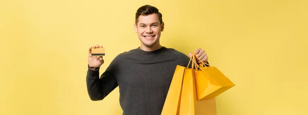 Smiling man with credit card and shopping bags on yellow background, banner — Stock Photo