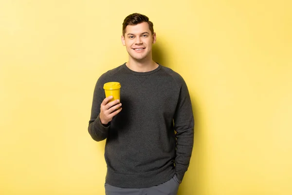 Sorrindo homem segurando copo de papel no fundo amarelo — Fotografia de Stock