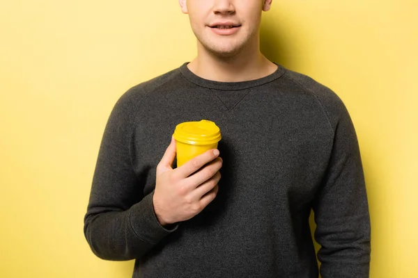 Обрезанный вид человека в сером свитере с одноразовой чашкой на желтом фоне — стоковое фото