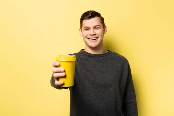 Улыбающийся мужчина держит бумажную чашку на размытом переднем плане на желтом фоне — стоковое фото