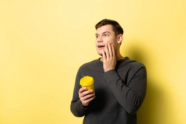 Aufgeregter Mann mit Pappbecher blickt auf gelbem Hintergrund weg — Stockfoto