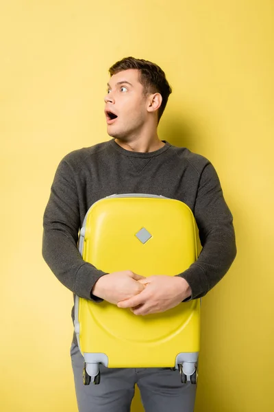 Homme étonnant avec bouche ouverte tenant valise sur fond jaune — Photo de stock