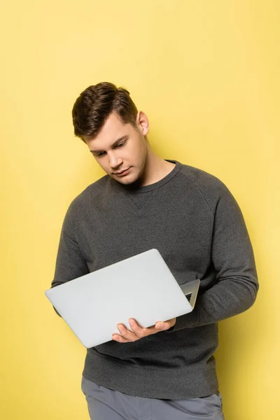 Young man using laptop on yellow background — Stock Photo