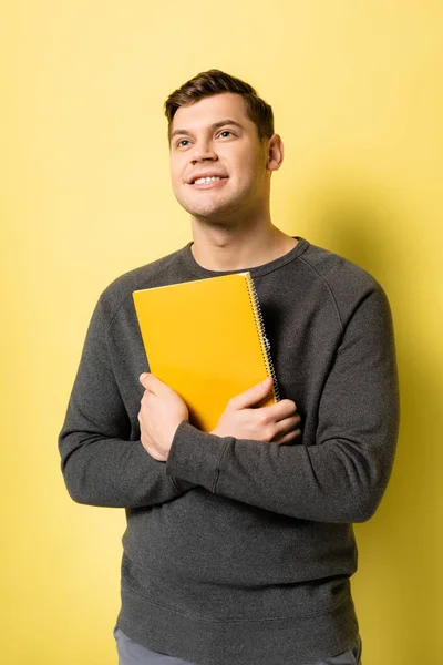 Smiling man looking up while holding notebook on yellow background — Stock Photo