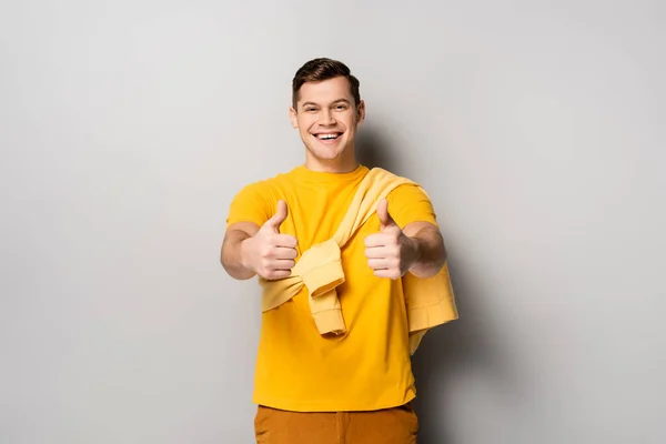 Sorrindo homem mostrando polegares para cima no fundo cinza — Fotografia de Stock