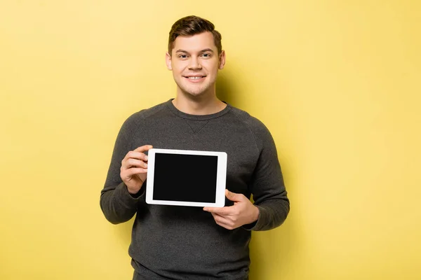 Uomo sorridente che tiene tablet digitale con schermo bianco su sfondo giallo — Foto stock