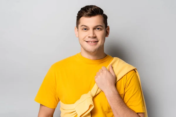 Веселый человек держит желтый пуловер на сером фоне — стоковое фото