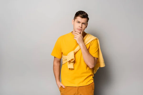 Pensive man looking at camera while standing on grey background — Stock Photo