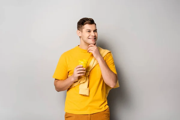 Hombre sonriente sosteniendo café para llevar sobre fondo gris - foto de stock