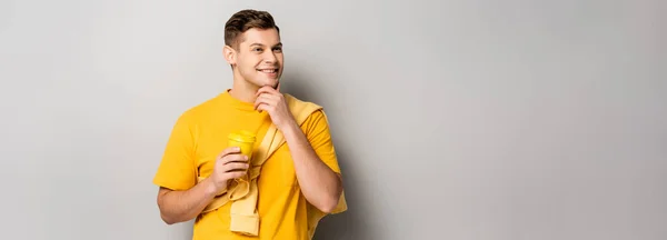 Uomo positivo in possesso di tazza di carta su sfondo grigio, banner — Foto stock