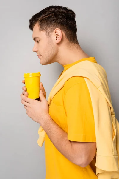 Vista lateral del hombre oliendo café para llevar sobre fondo gris - foto de stock