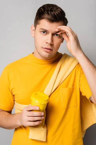 Man looking at camera while holding takeaway drink on grey background — Stock Photo