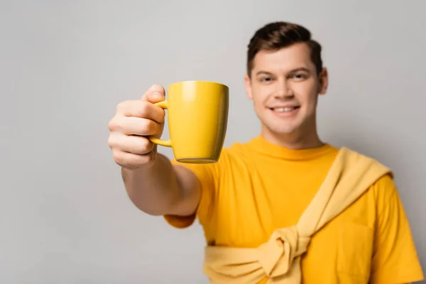 Taza amarilla en la mano del hombre sonriente borrosa sobre fondo gris - foto de stock