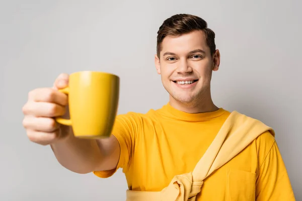 Hombre positivo sosteniendo taza en primer plano borroso sobre fondo gris - foto de stock