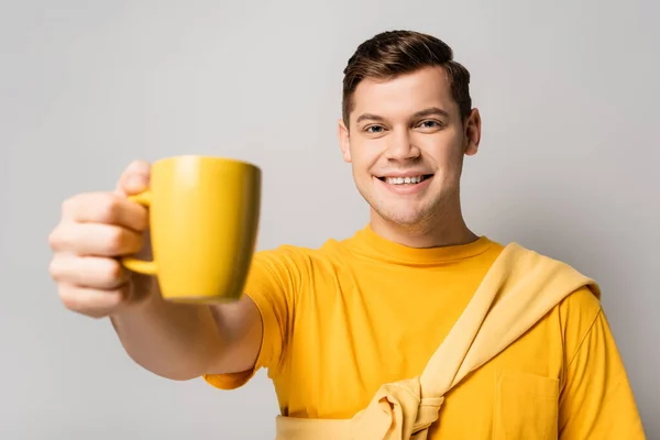 Homme positif tenant une tasse sur fond gris au premier plan flou — Photo de stock