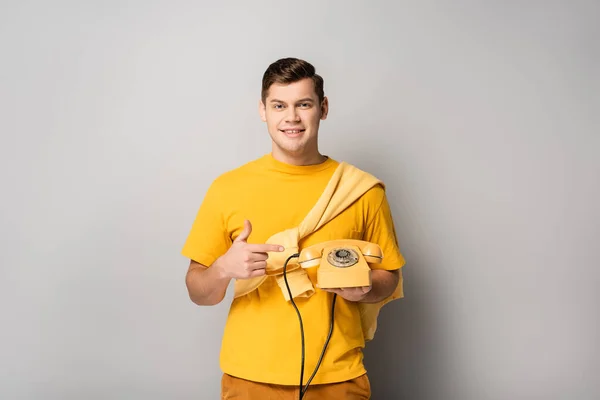 Hombre sonriente señalando el teléfono amarillo sobre fondo gris - foto de stock