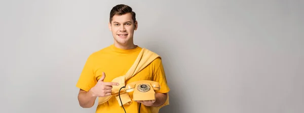 Man pointing at yellow vintage telephone on grey background, banner — Stock Photo