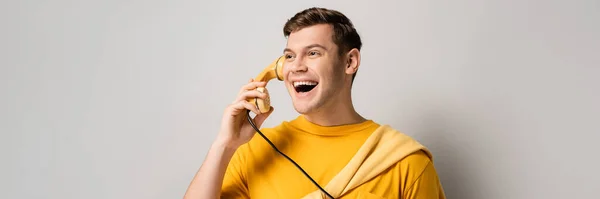 Молодой счастливый человек разговаривает по телефону на сером фоне, баннер — стоковое фото