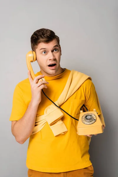 Uomo stupito guardando in alto mentre parla al telefono su sfondo grigio — Foto stock