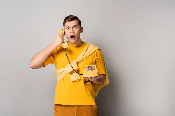 Homme étonné avec bouche ouverte parlant sur un téléphone vintage sur fond gris — Photo de stock