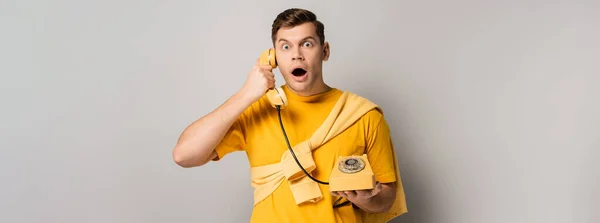 Young man with open mouth talking on telephone on grey background, banner — Stock Photo