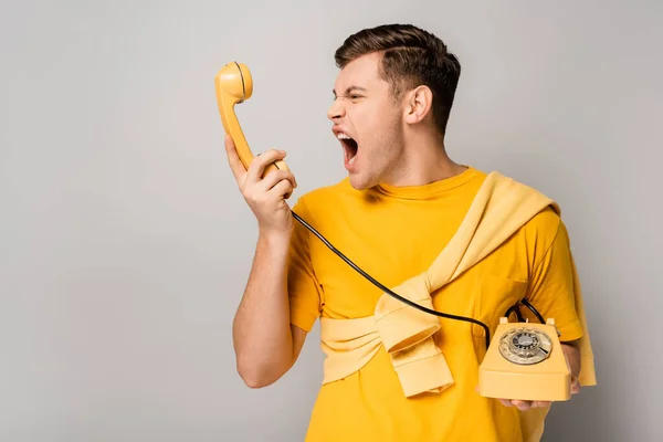 Злий чоловік кричить по телефону на сірому фоні — стокове фото