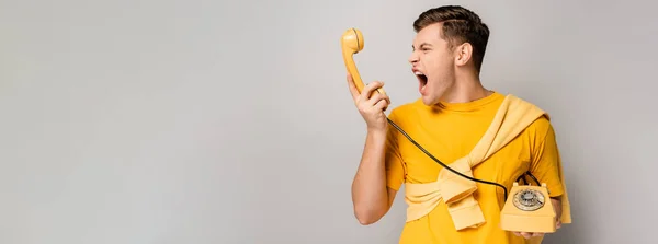 Aggressive man screaming at yellow telephone handset on grey background, banner — Stock Photo