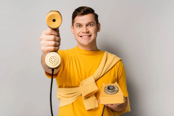 Hombre alegre sosteniendo el auricular del teléfono en primer plano borroso sobre fondo gris - foto de stock