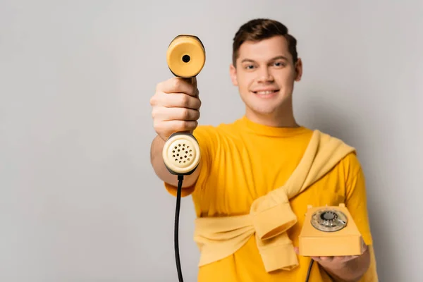 Auricular amarillo del teléfono en la mano del hombre sonriente borroso sobre fondo gris - foto de stock