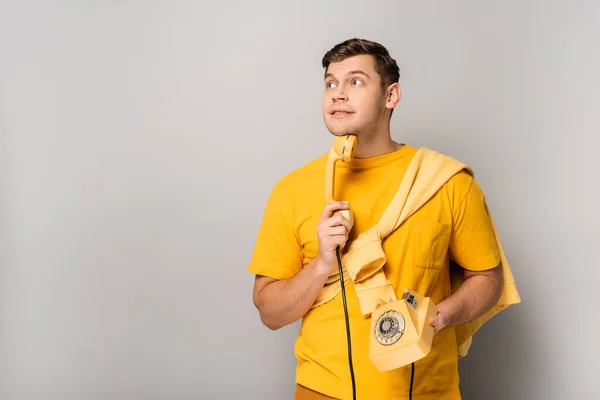 Hombre de ensueño sosteniendo teléfono vintage sobre fondo gris - foto de stock