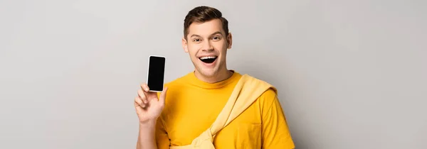 Positive man holding smartphone with blank screen on grey background, banner — Stock Photo