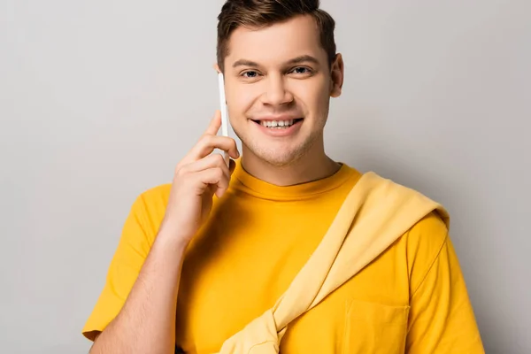 Homme souriant parlant sur un téléphone portable et regardant la caméra sur fond gris — Photo de stock