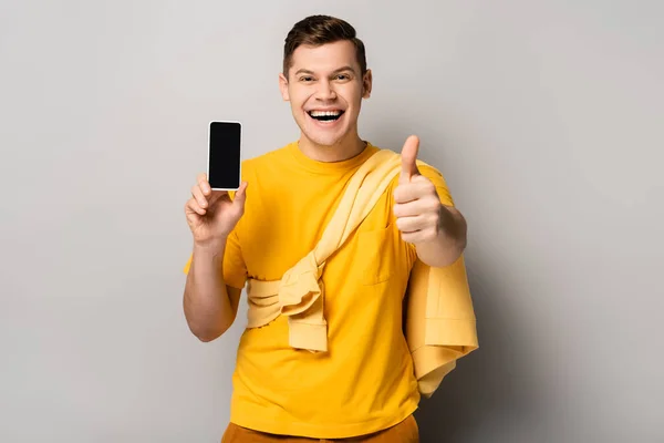 Fröhlicher Mann zeigt wie und hält Handy mit leerem Bildschirm auf grauem Hintergrund — Stockfoto