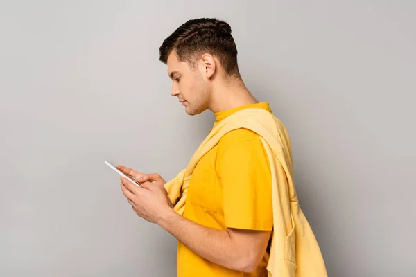 Vue latérale de l'homme en t-shirt jaune avec smartphone sur fond gris — Photo de stock