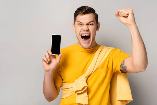 Aufgeregter Mann zeigt Yah-Geste und hält Smartphone mit leerem Bildschirm auf grauem Hintergrund — Stockfoto