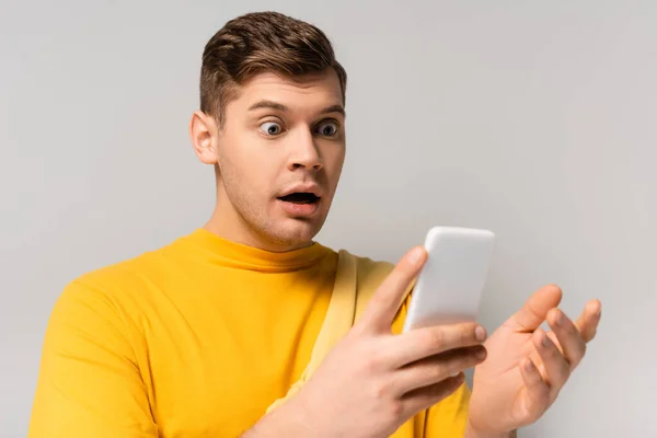 Homme étonnant en utilisant un téléphone portable sur le premier plan flou sur fond gris — Photo de stock