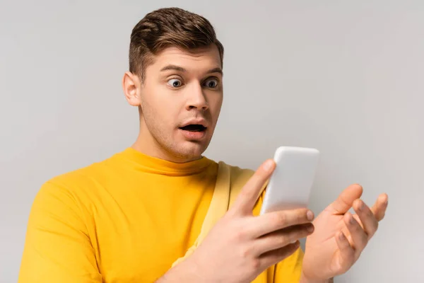Uomo stupito utilizzando il cellulare in primo piano sfocato su sfondo grigio — Foto stock