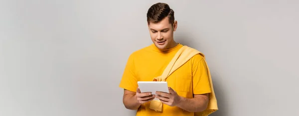 Jeune homme utilisant une tablette numérique sur fond gris, bannière — Photo de stock