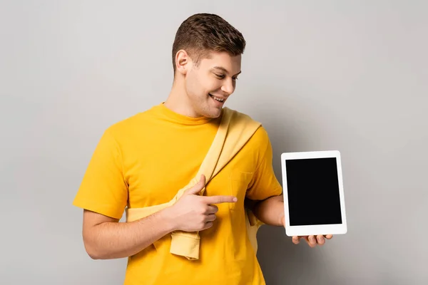 Hombre sonriente apuntando a la tableta digital con pantalla en blanco sobre fondo gris - foto de stock