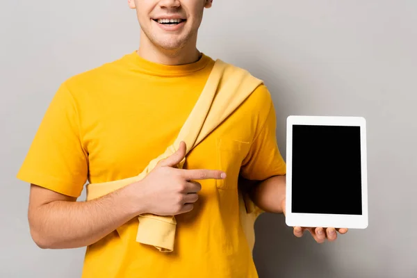Обрезанный вид веселого человека, указывающего пальцем на цифровой планшет с пустым экраном на сером фоне — стоковое фото