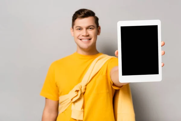 Comprimido digital com tela em branco na mão do homem sorridente borrado em fundo cinza — Fotografia de Stock