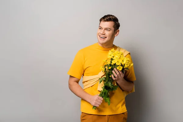 Веселий чоловік тримає жовті квіти на сірому фоні — стокове фото