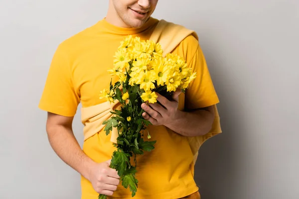 Vista recortada del hombre sonriente sosteniendo ramo de crisantemos sobre fondo gris - foto de stock