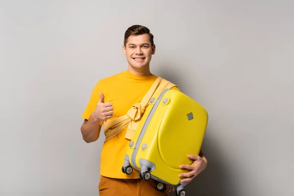 Tourist with suitcase showing thumb up on grey background — Stock Photo