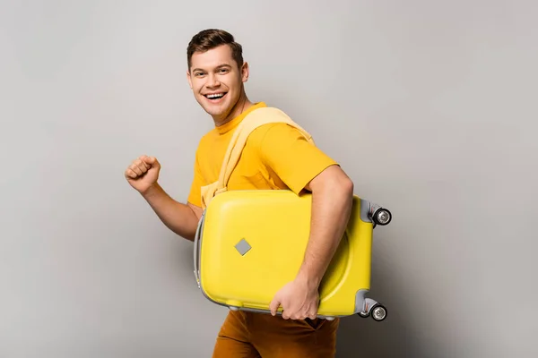 Hombre feliz con maleta mirando a la cámara sobre fondo gris - foto de stock