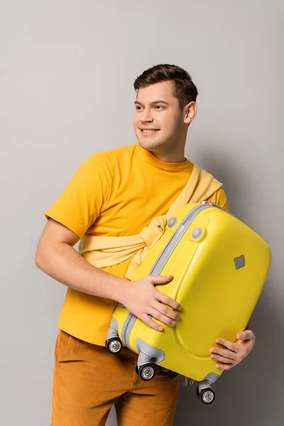 Young man in casual clothes holding suitcase on grey background — Stock Photo