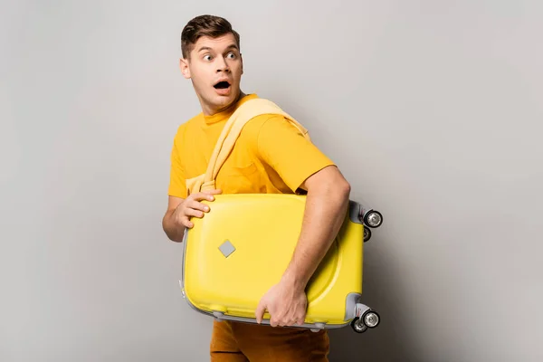 Amazed tourist with open mouth holding suitcase on grey background — Stock Photo