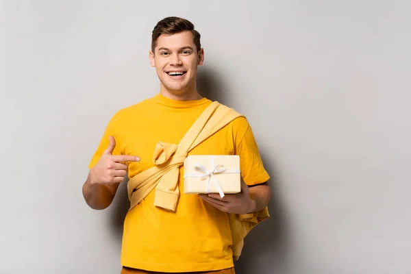 Lächelnder Mann zeigt derzeit mit dem Finger mit Schleife auf grauem Hintergrund — Stockfoto