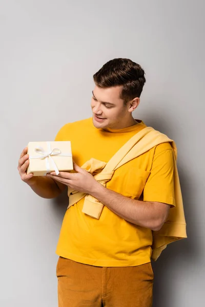 Morena hombre en ropa casual mirando regalo sobre fondo gris - foto de stock