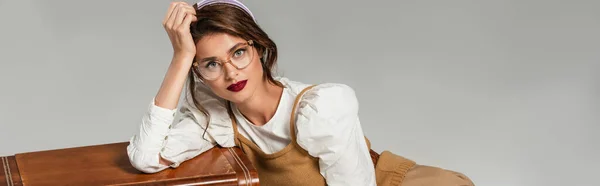 Mujer joven y elegante en ropa retro apoyada en el receptor de radio vintage aislado en gris, pancarta - foto de stock